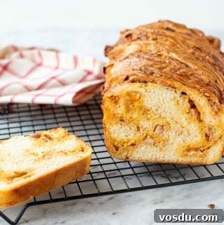 Cross section of cheese filled Bread loaf on black wire rack with a slice of bread on the side and red and white cloth in the background