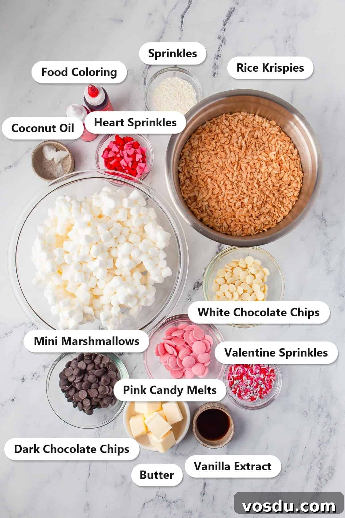 Labeled ingredients for Valentine rice krispie treats including Rice Krispies, mini marshmallows, butter, vanilla extract, white chocolate chips, pink candy melts, dark chocolate chips, coconut oil, food coloring, and sprinkles.