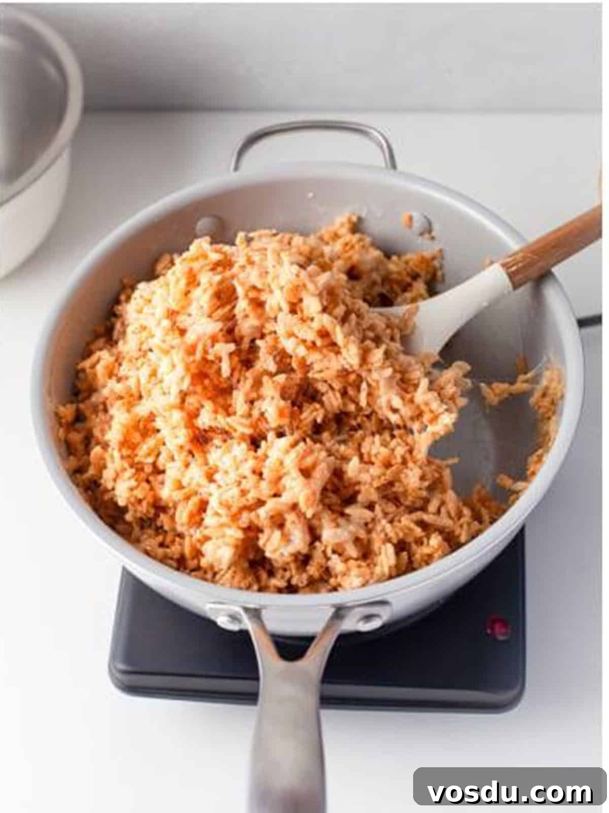 Rice Krispies cereal stirred into the melted marshmallow mixture in a saucepan.