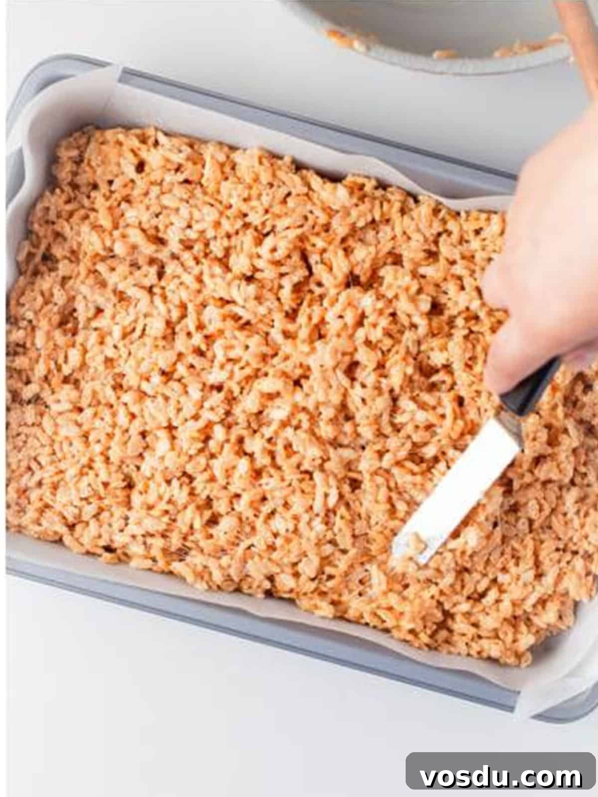 Rice krispie mixture pressed evenly into a parchment lined 9x13 baking pan with a spatula.