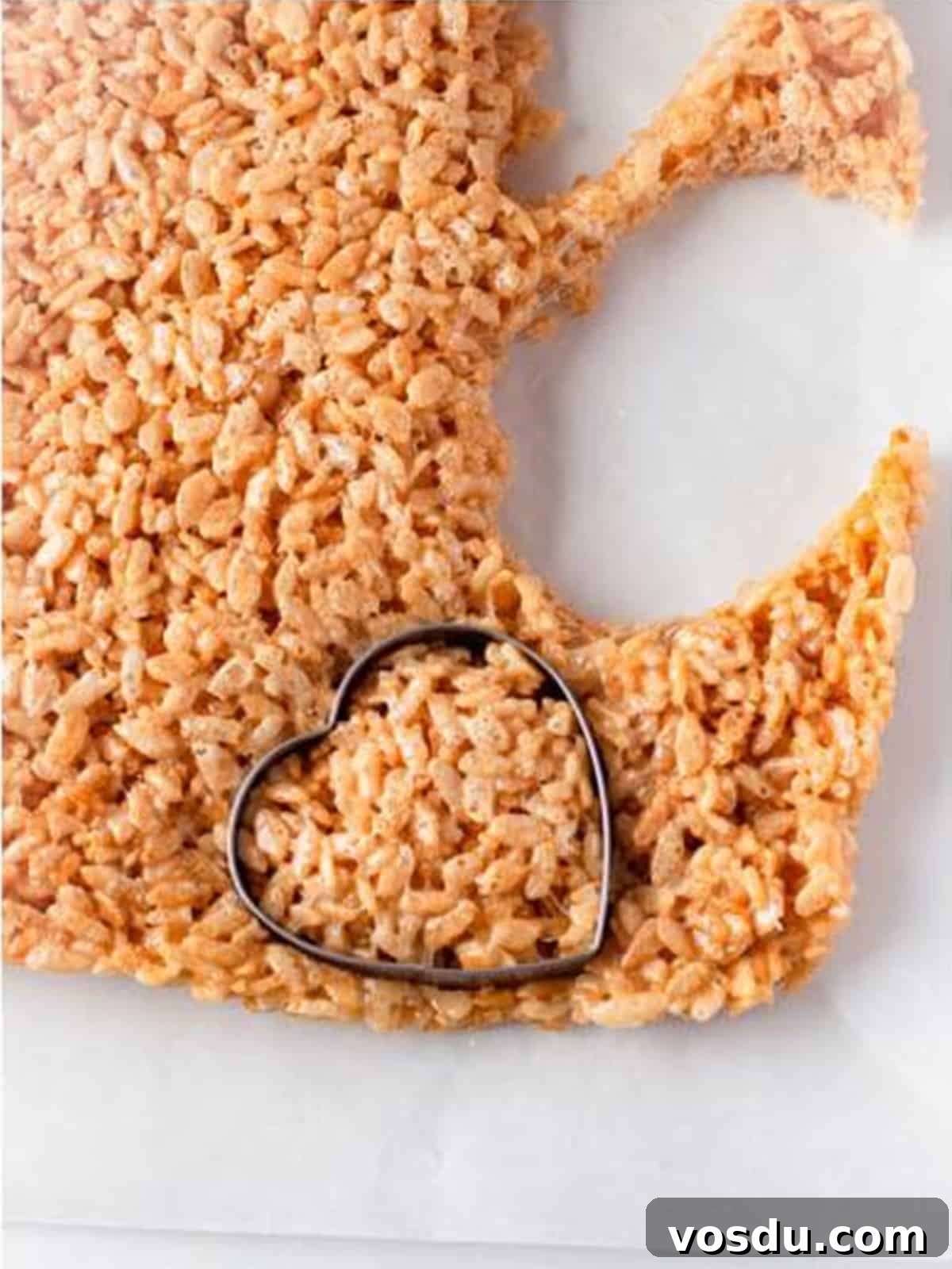 Heart shaped cookie cutter cutting hearts out of the slab of rice krispie treats.