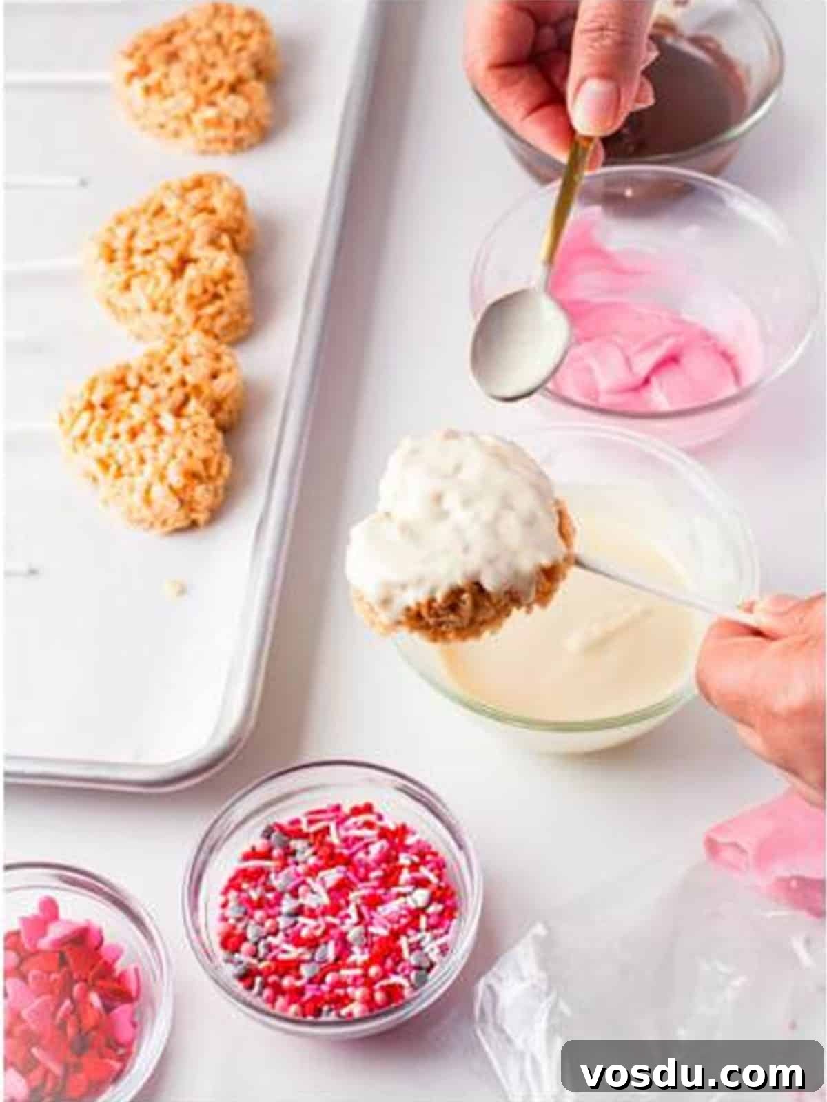 Rice krispie treat heart on a stick being dipped into melted white chocolate with a spoon.