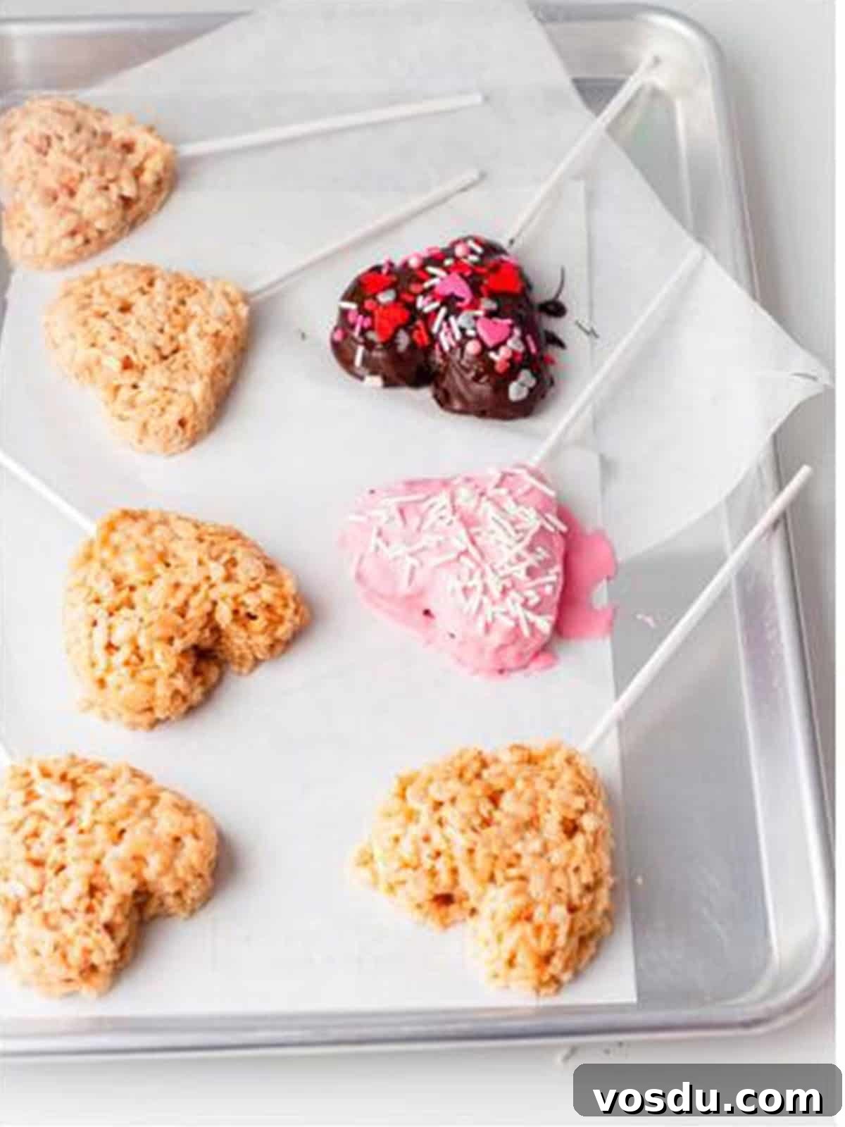 Chocolate dipped Valentine rice krispie treat hearts decorated with sprinkles setting on parchment paper.