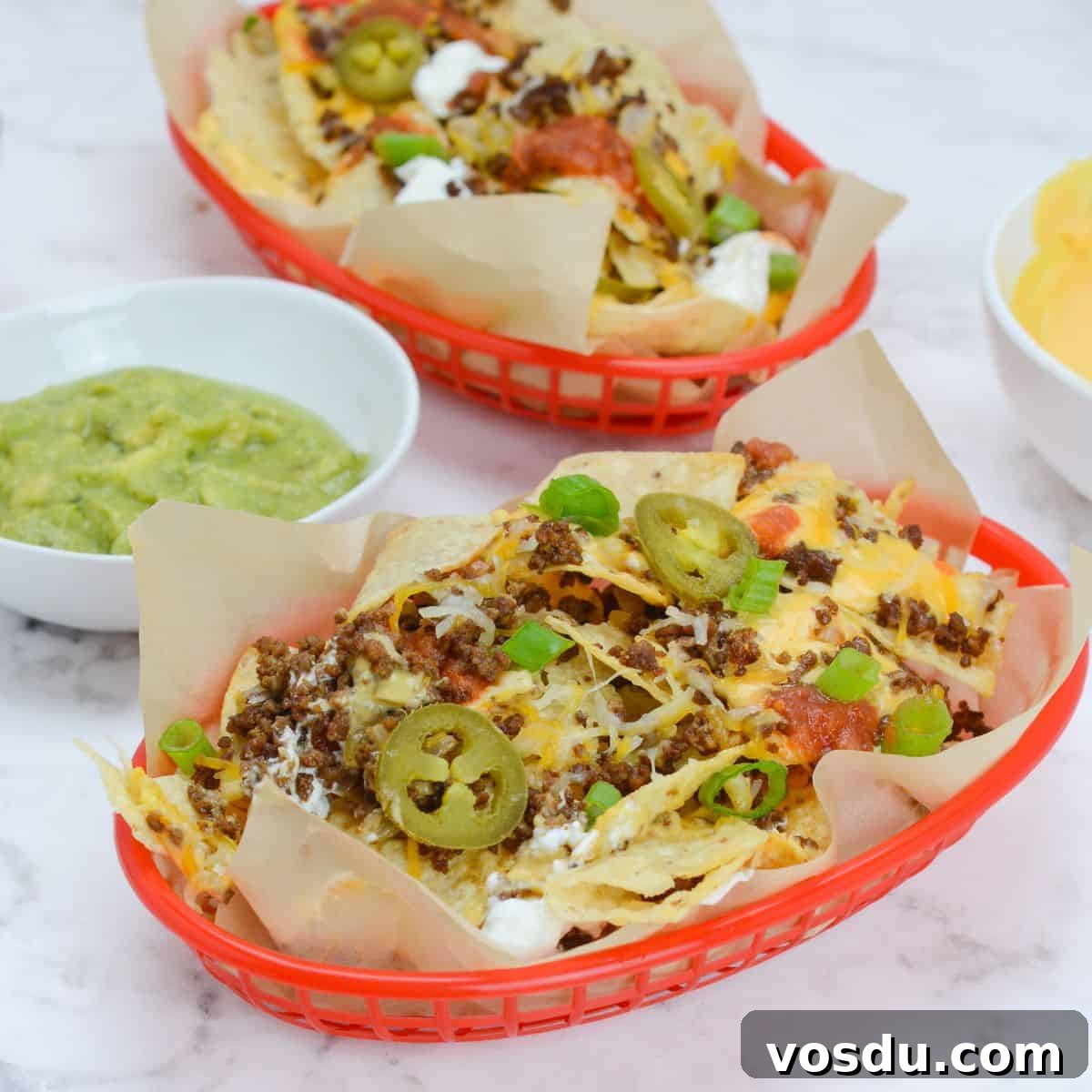 two baskets of blackstone nachos with a variety of toppings.