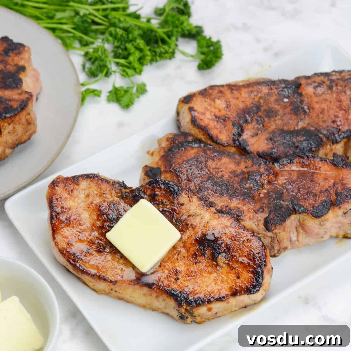 finished blackstone pork chops, plated on a white platter and topped with butter