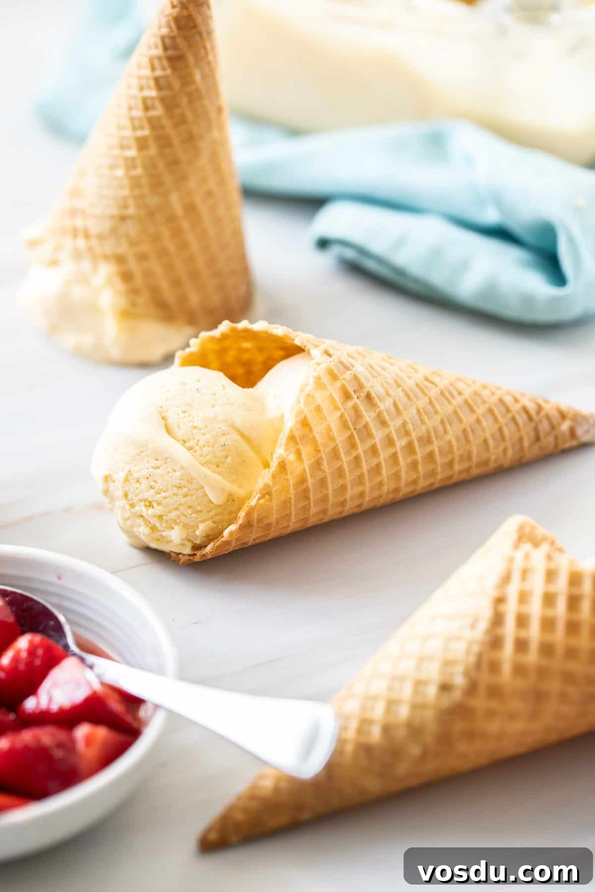 Three ice cream cones, one with ice cream in it, with a bowl of strawberries on the side.