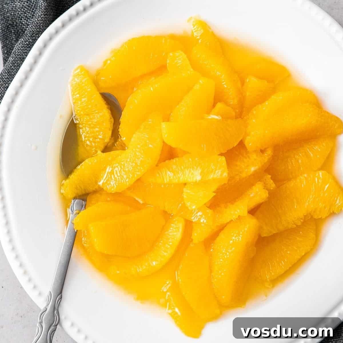 Round white dish, full of brandied oranges, with a spoon sitting in the dish.