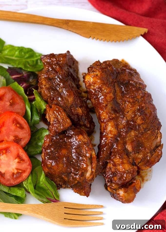 Two Country Style Ribs on a white plate with vegetables and a wooden fork and knife