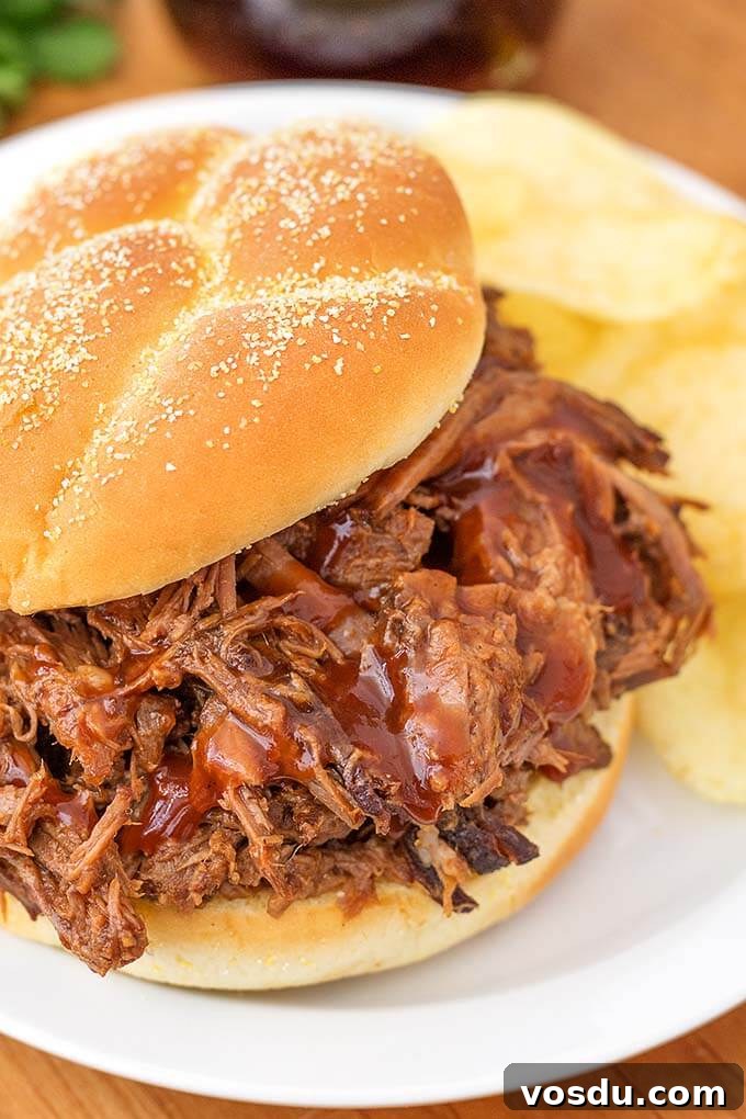 Barbecue Beef on a hamburger bun and potato chips on a white plate