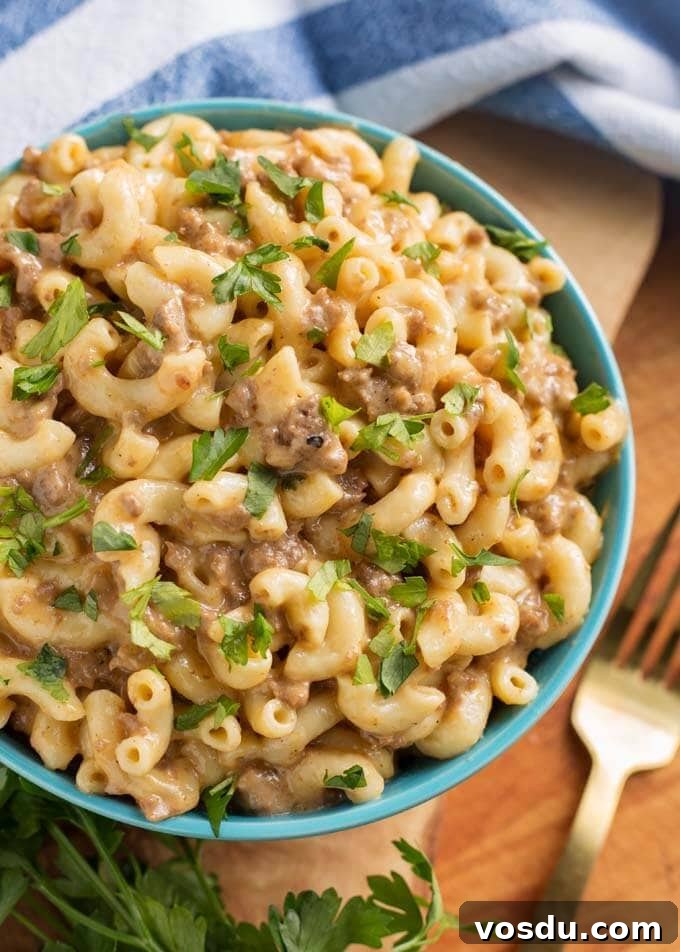 Cheeseburger Macaroni in a blue bowl next to fork all on wooden board
