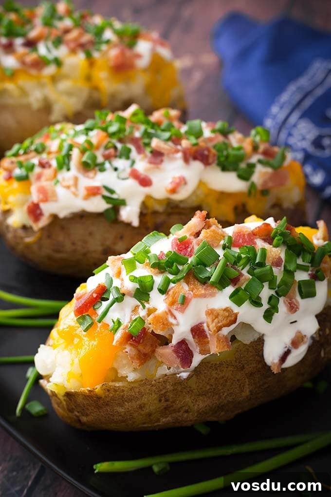 Three Baked Potato topped with cheese, bacon, sour cream and chives on wooden board with green onions