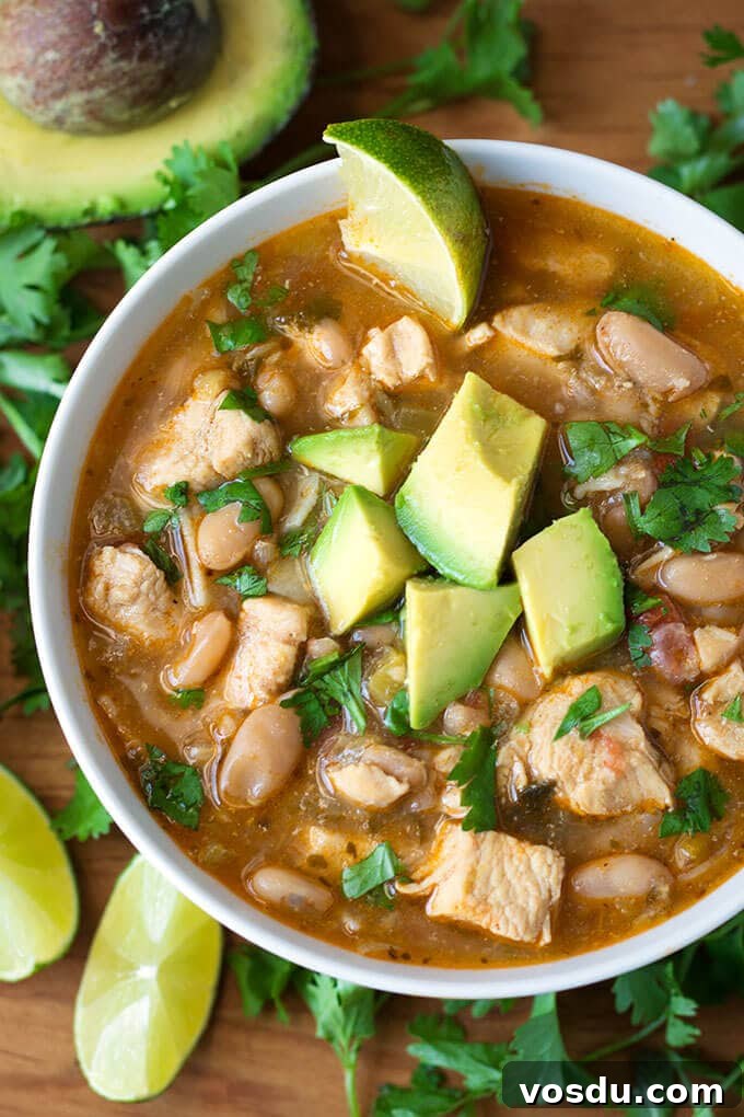  White Chicken Chili in a white bowl garnished with cubed avocados and cilantro
